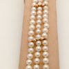 A woman holding 3 Row South Sea Cultured Pearls 8mm 18k Yellow Gold Clasp w/ VS Diamonds accents on a platform