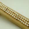 A woman holding 3 Row South Sea Cultured Pearls 8mm 18k Yellow Gold Clasp w/ VS Diamonds accents on a platform