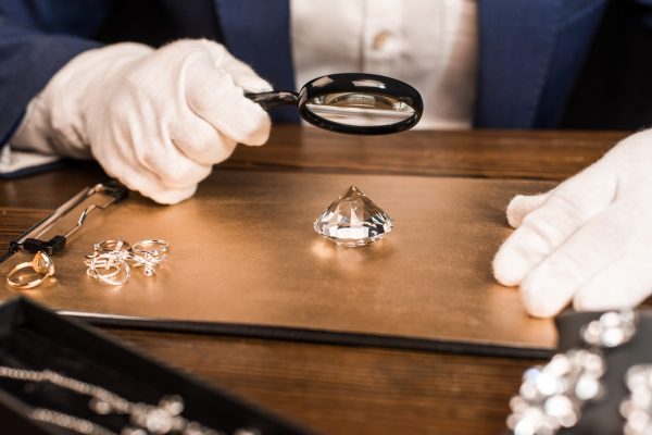 Cropped view of jewelry appraiser examining gemstone with magnifying glass near jewelry on board on